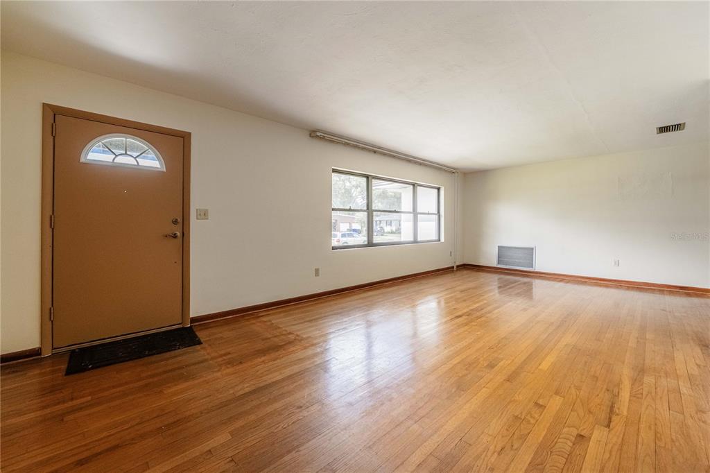 An empty living room features hardwood floors, a tan front door, and a large window — 521 BONNIE DRIVE, LAKELAND, FL