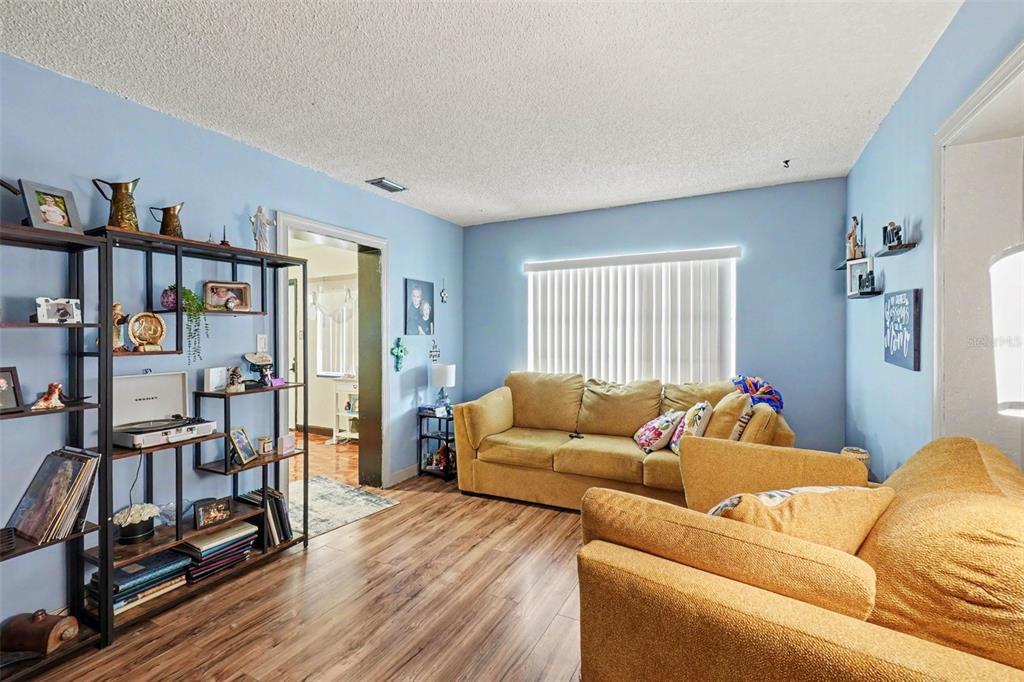 A living room features blue walls, wood-look flooring, a yellow sofa, and a metal shelving unit — 3040 STRAWBERRY LANE, LAKELAND, FL