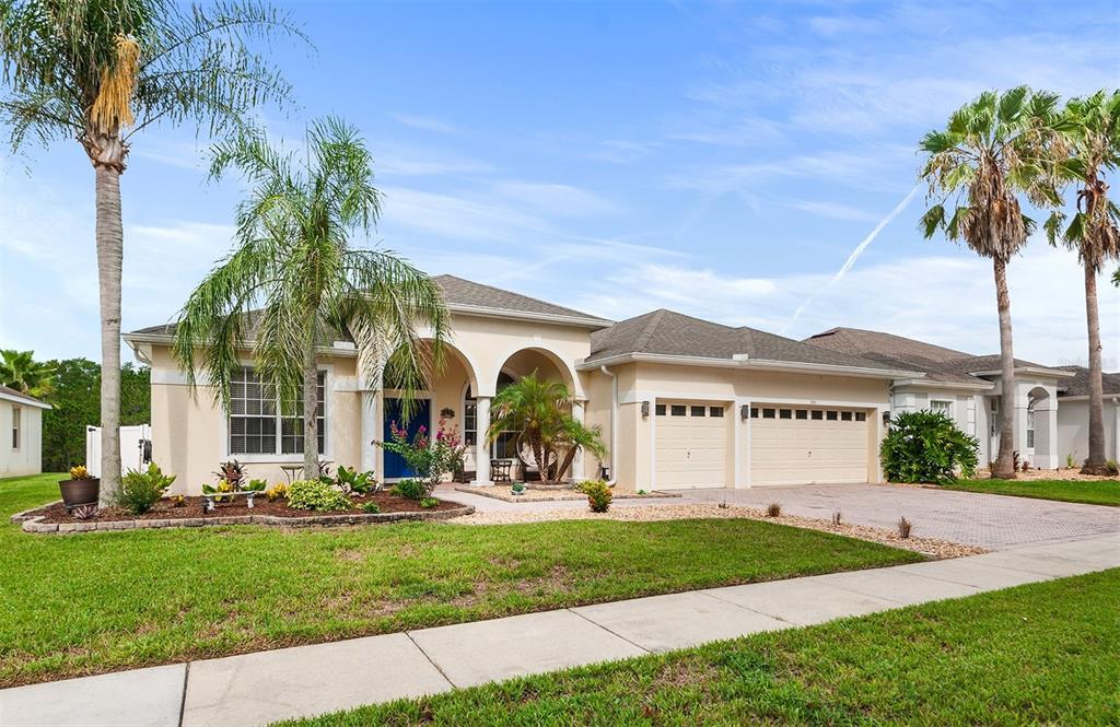 A single-story tan stucco house with a two-car garage and palm trees in the yard — 301 BIRKDALE STREET, DAVENPORT, FL