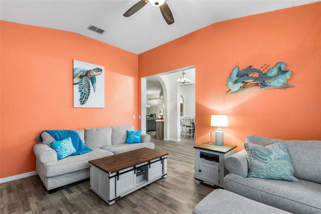 A living room features orange walls, gray sofas, a wood-topped coffee table, and coastal decor — 301 BIRKDALE STREET, DAVENPORT, FL