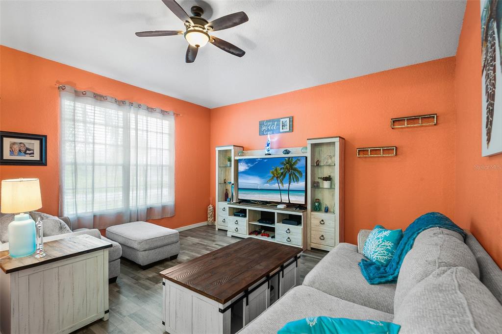 A living room features bright orange walls, a ceiling fan, and a television entertainment center — 301 BIRKDALE STREET, DAVENPORT, FL