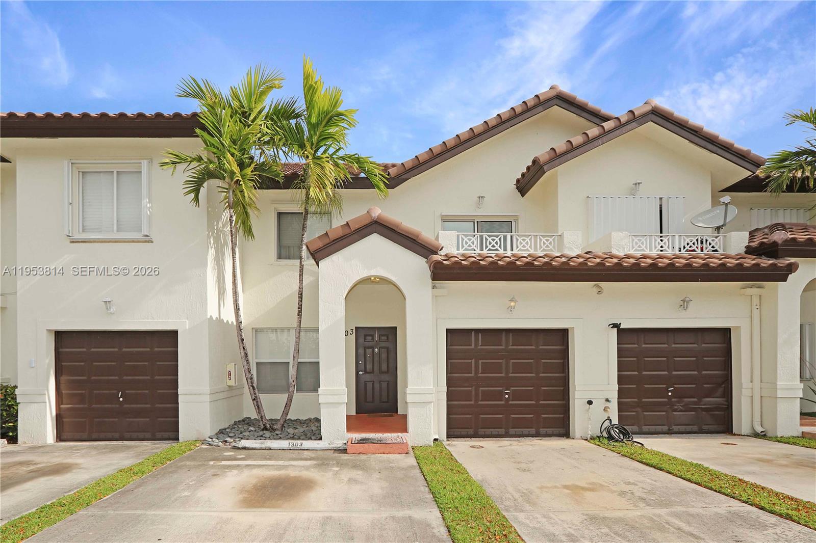 A two-story townhouse exterior features a brown tiled roof, three garage doors, and palm trees — 10921 NW 88th Ter # 1303, Doral FL 33178, DORAL, FL