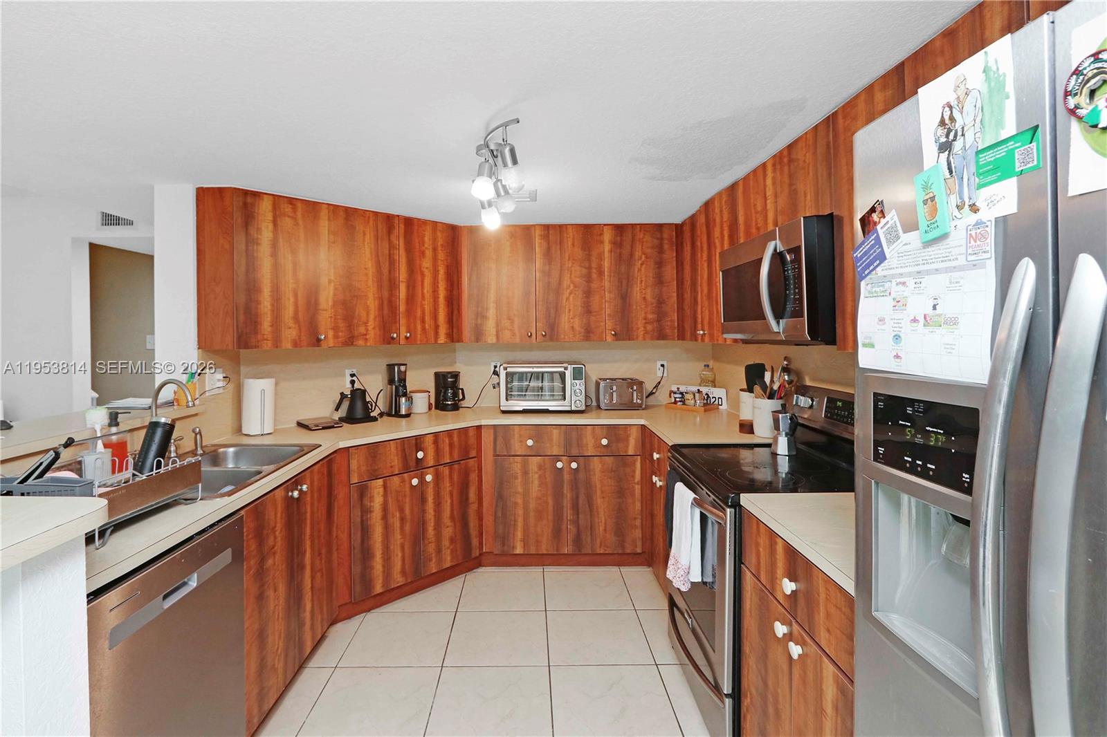 A kitchen features wood-grain cabinets, stainless steel appliances, and light-colored tile flooring — 10921 NW 88th Ter # 1303, Doral FL 33178, DORAL, FL