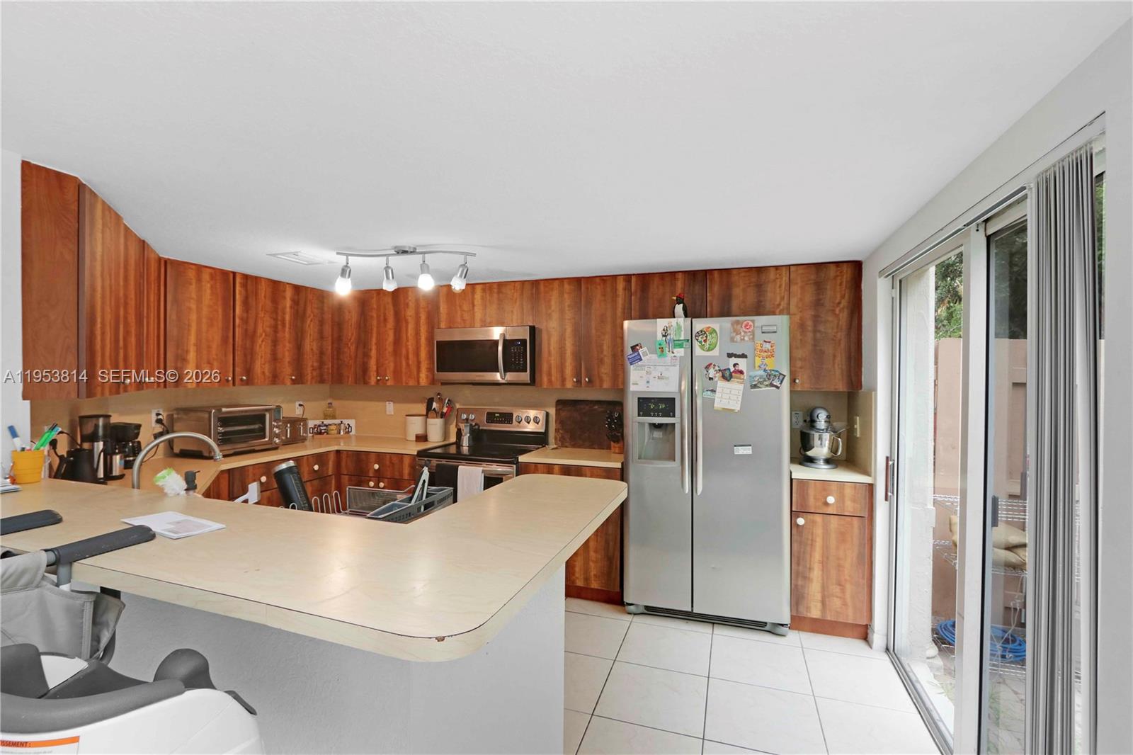 A kitchen features wood-grain cabinets, stainless steel appliances, a breakfast bar, and sliding glass doors — 10921 NW 88th Ter # 1303, Doral FL 33178, DORAL, FL