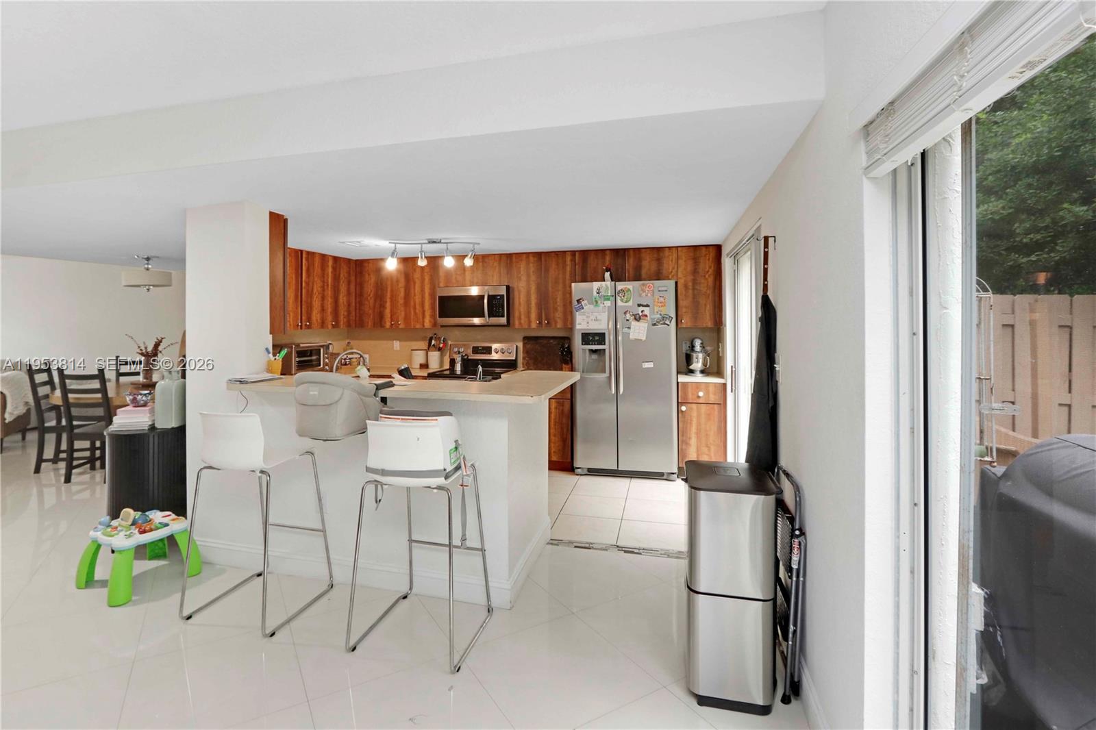 A kitchen features wood cabinets, stainless steel appliances, a breakfast bar, and white tile flooring — 10921 NW 88th Ter # 1303, Doral FL 33178, DORAL, FL
