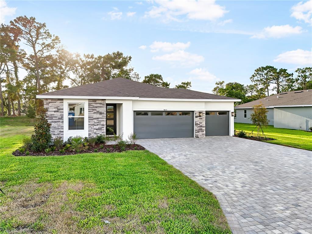A single-story house with a stone facade, gray garage doors, and a paved driveway — 9127 PLAYERS DRIVE, WEEKI WACHEE, FL