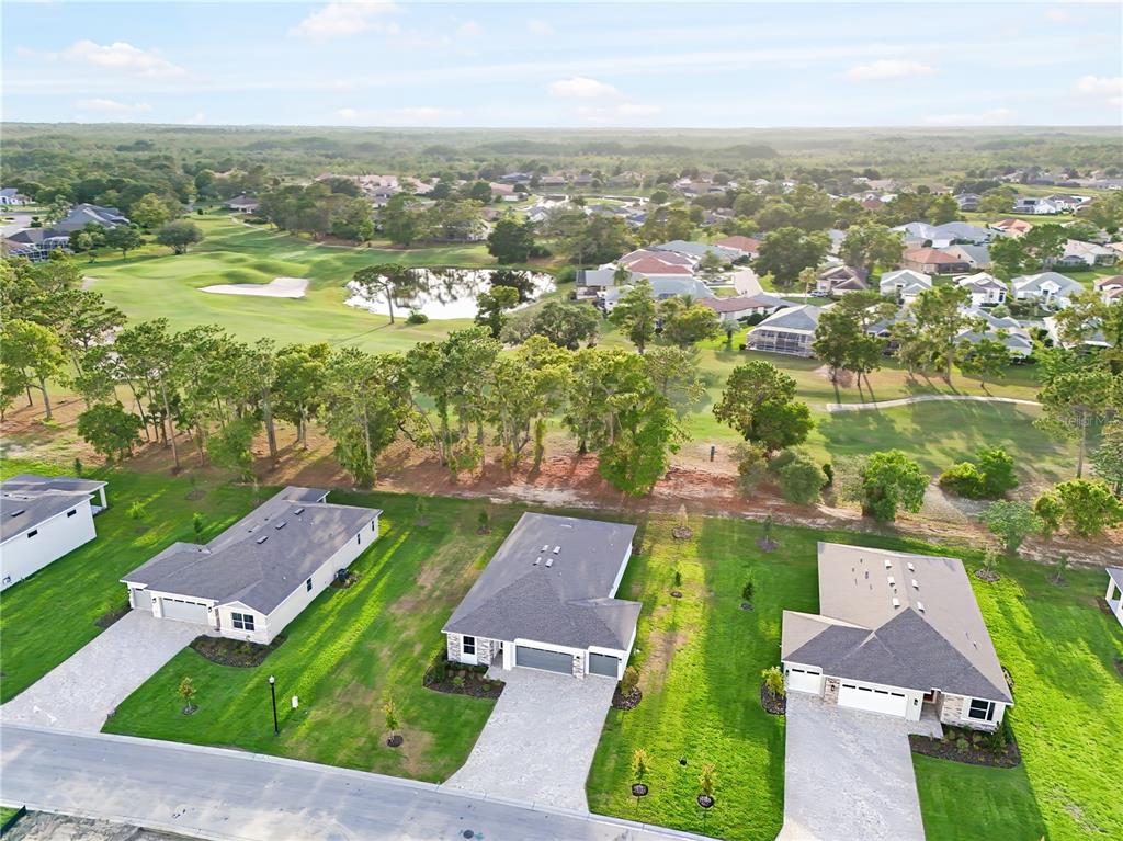 An aerial view shows three suburban houses with driveways facing a golf course and pond — 9127 PLAYERS DRIVE, WEEKI WACHEE, FL
