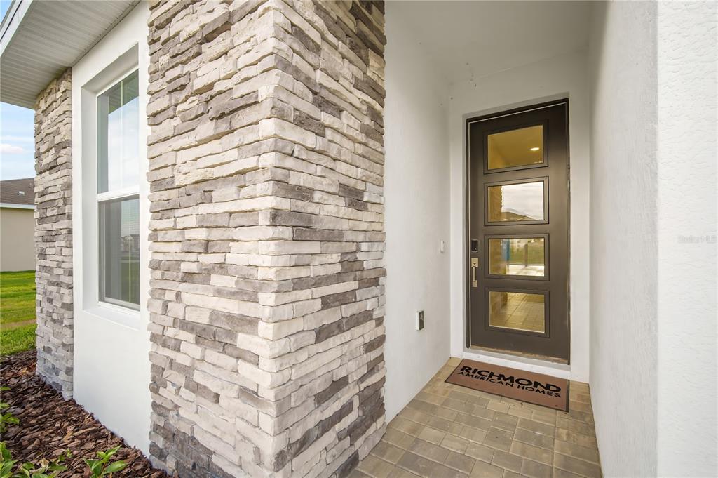 A front entryway features a stone-clad corner, a dark door with glass panels, and pavers — 9127 PLAYERS DRIVE, WEEKI WACHEE, FL