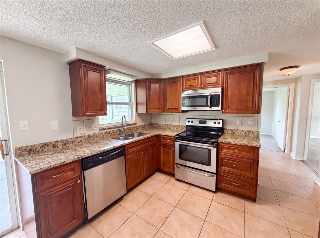 A kitchen features wood cabinets, granite countertops, stainless steel appliances, and tile flooring — 3518 GORMAN DRIVE, NEW PORT RICHEY, FL