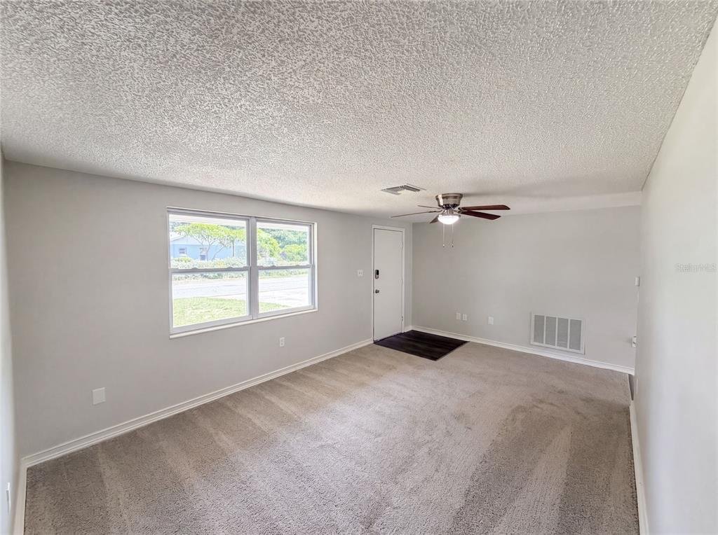 An empty living room features light gray walls, beige carpeting, a ceiling fan, and a window — 3518 GORMAN DRIVE, NEW PORT RICHEY, FL