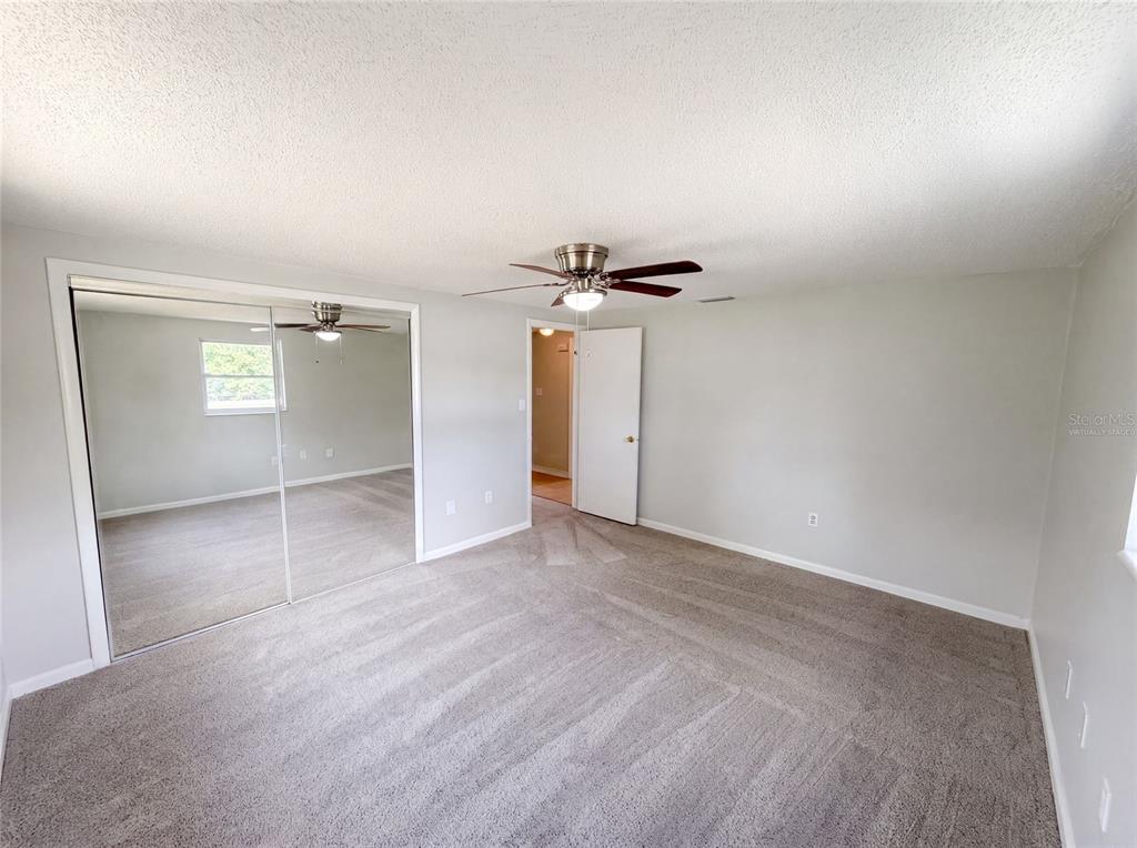 A bedroom with gray carpet, light gray walls, a ceiling fan, and mirrored closet doors — 3518 GORMAN DRIVE, NEW PORT RICHEY, FL