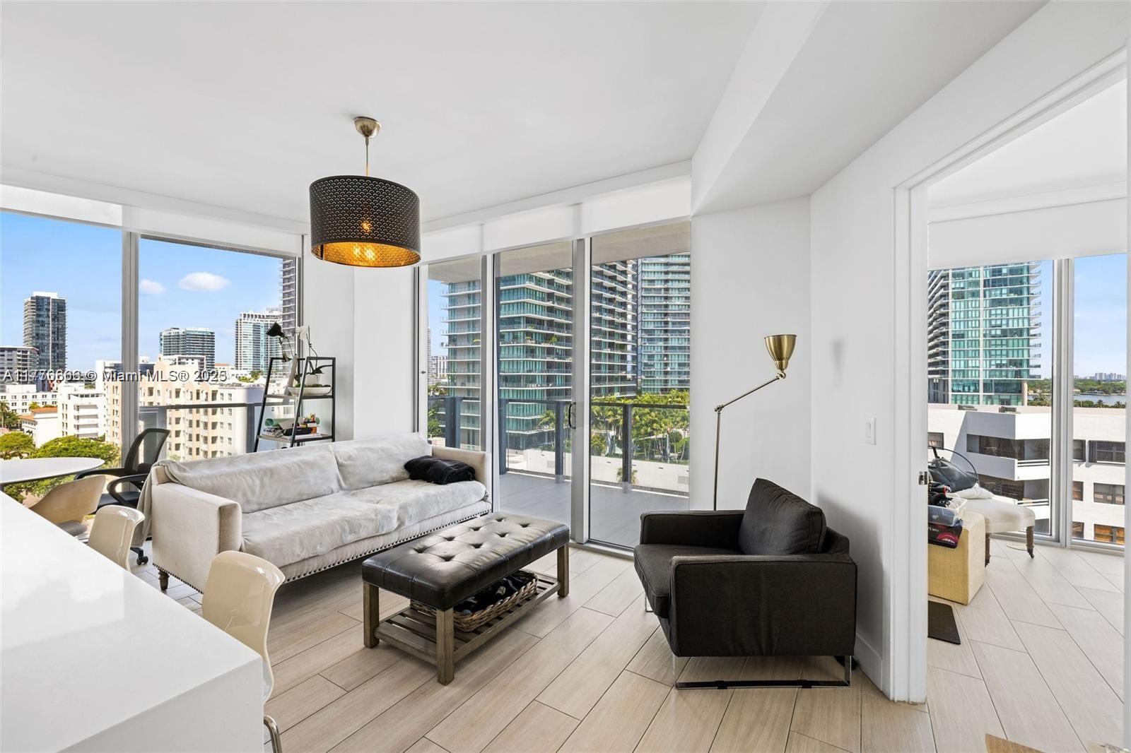 A modern living room features a light sofa, dark armchair, and floor-to-ceiling windows overlooking city buildings — 2900 NE 7th Ave # 901, Miami FL 33137, MIAMI, FL