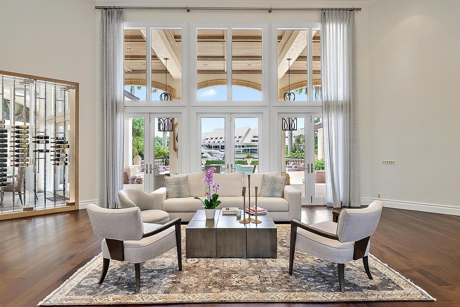 A living room features a large wine display, floor-to-ceiling windows, and a view of a pool — 193 Spyglass Court, Jupiter FL 33477, JUPITER, FL