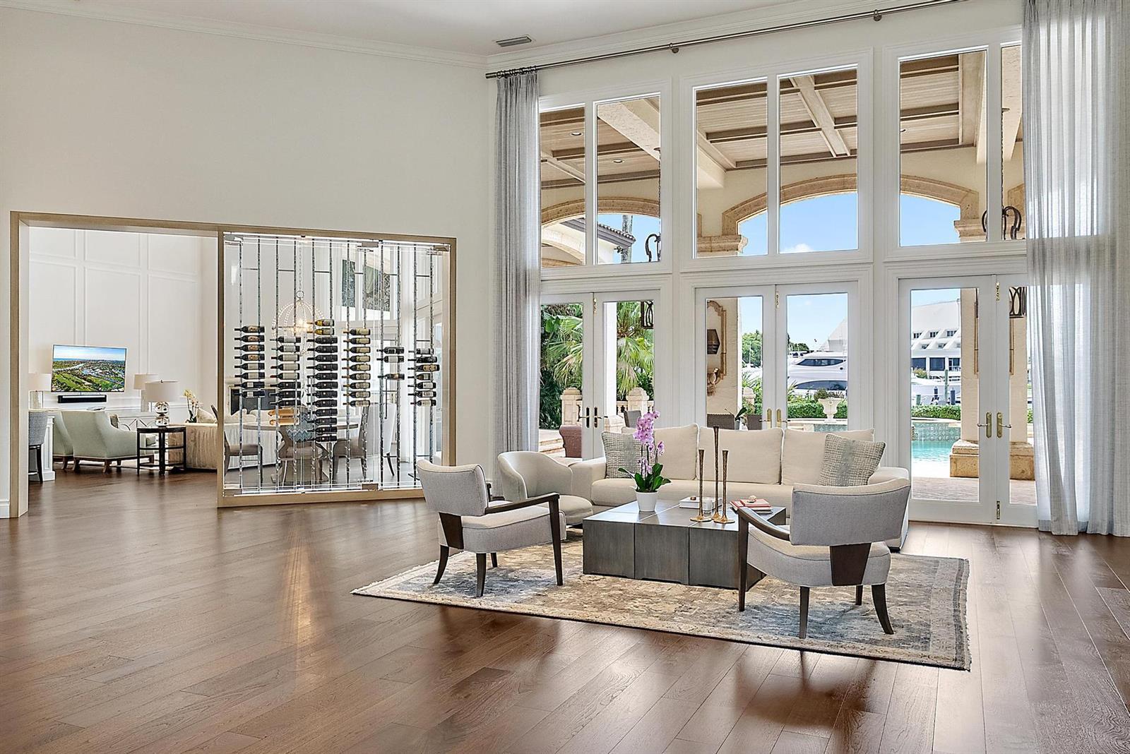 A spacious living room features a glass wine display, floor-to-ceiling windows, and pool views — 193 Spyglass Court, Jupiter FL 33477, JUPITER, FL