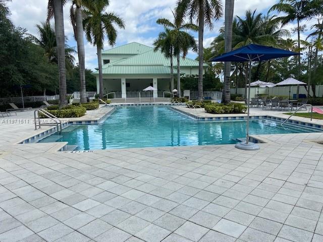A swimming pool with a blue umbrella sits in front of a large clubhouse building — 5300 NW 87th Ave # 316, Doral FL 33178, DORAL, FL