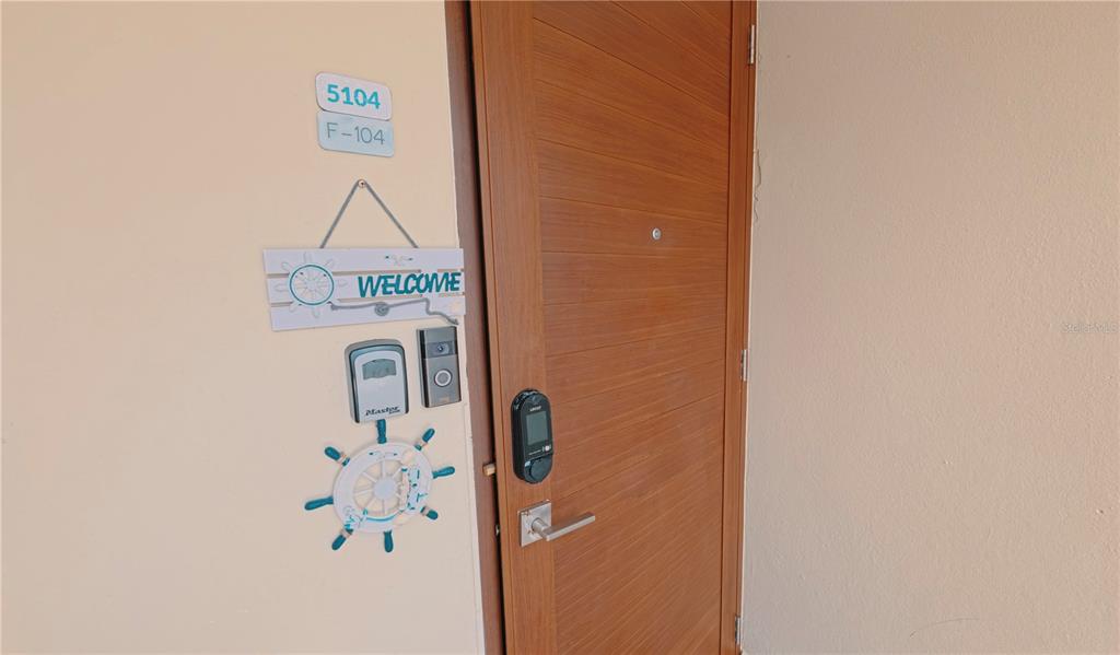A wooden front door features a digital lock, a key lockbox, and a nautical-themed welcome sign — 400 COND. HAUDIMAR BEACH APARTMENTS, EDIF. F UNIT F104, ISABELA, PR