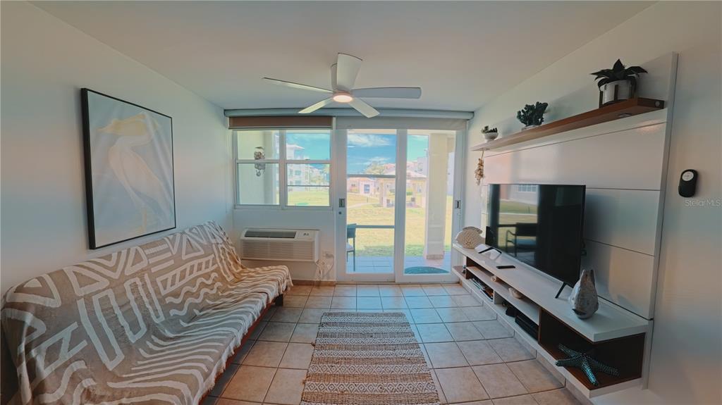 A living room features a patterned sofa, a wall-mounted television, and a sliding glass door — 400 COND. HAUDIMAR BEACH APARTMENTS, EDIF. F UNIT F104, ISABELA, PR