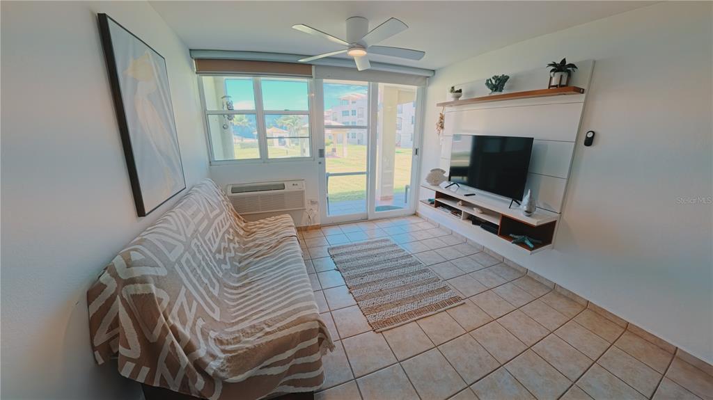 A living room features a patterned sofa, a wall-mounted television, and tile flooring — 400 COND. HAUDIMAR BEACH APARTMENTS, EDIF. F UNIT F104, ISABELA, PR