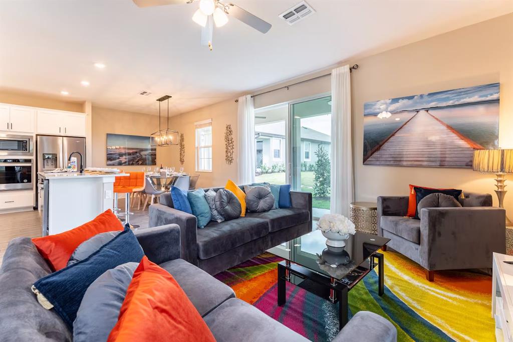 A living room with gray sofas, a colorful rug, and an open kitchen area — 7951 HAVERHILL WAY, KISSIMMEE, FL