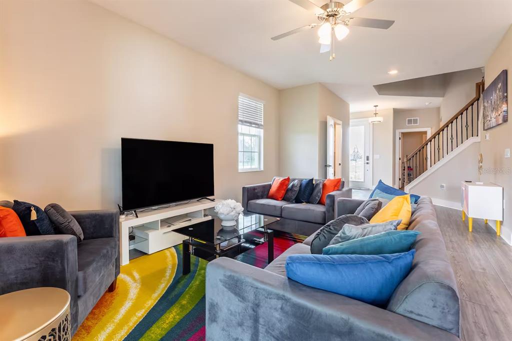 A living room features gray sofas, a colorful area rug, and a television on a stand — 7951 HAVERHILL WAY, KISSIMMEE, FL