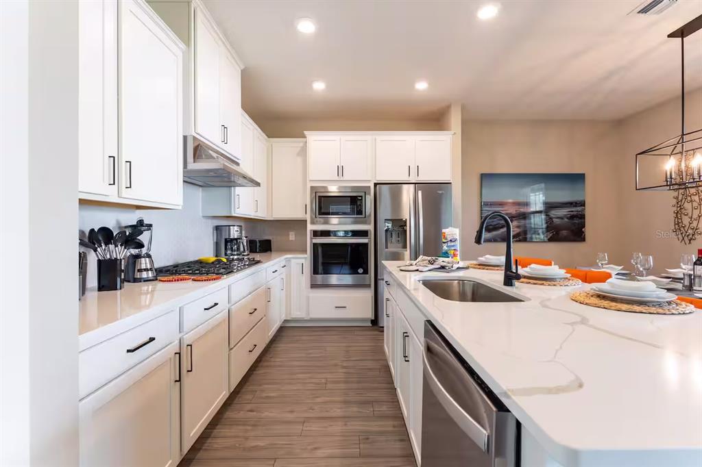 A modern kitchen features white cabinets, stainless steel appliances, and a large quartz-topped island — 7951 HAVERHILL WAY, KISSIMMEE, FL