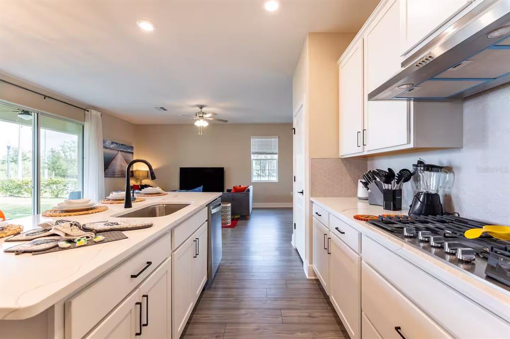 A modern kitchen with white cabinets and a large island overlooks an open living area — 7951 HAVERHILL WAY, KISSIMMEE, FL