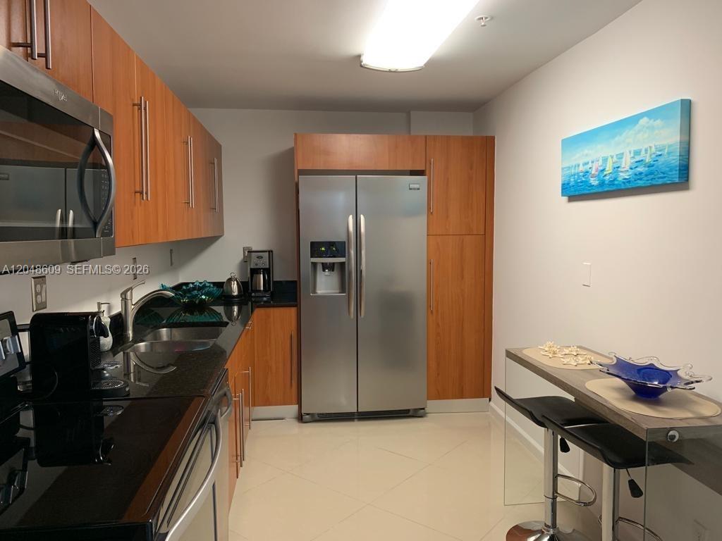 A kitchen features wood cabinets, stainless steel appliances, black countertops, and a small dining area — 3001 S Ocean Dr # 721, Hollywood FL 33019, HOLLYWOOD, FL