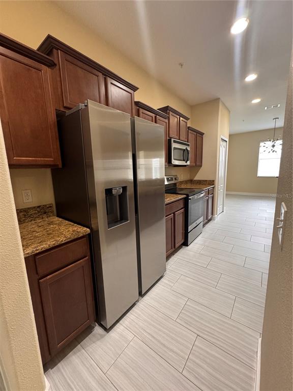A kitchen features dark wood cabinets, granite countertops, stainless steel appliances, and light tile flooring — 15511 CAMPDEN STREET, WINTER GARDEN, FL