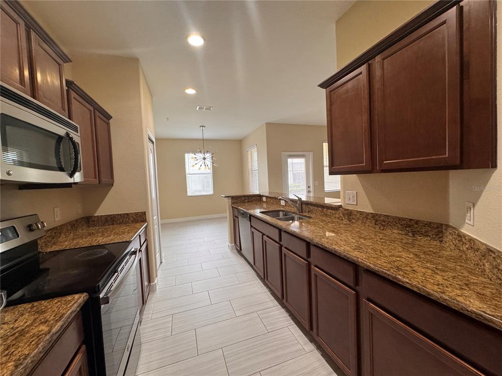 A kitchen features dark wood cabinets, granite countertops, stainless steel appliances, and light tile flooring — 15511 CAMPDEN STREET, WINTER GARDEN, FL