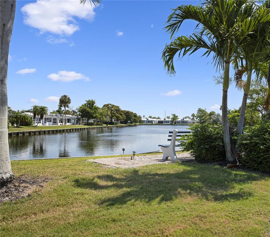 A grassy backyard features a stone patio with a bench overlooking a canal and houses — 524 SPANISH DRIVE S UNIT 125, LONGBOAT KEY, FL