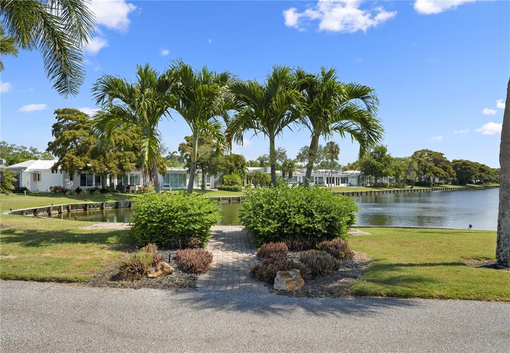 A brick path leads through a grassy yard toward a canal lined with palm trees — 524 SPANISH DRIVE S UNIT 125, LONGBOAT KEY, FL
