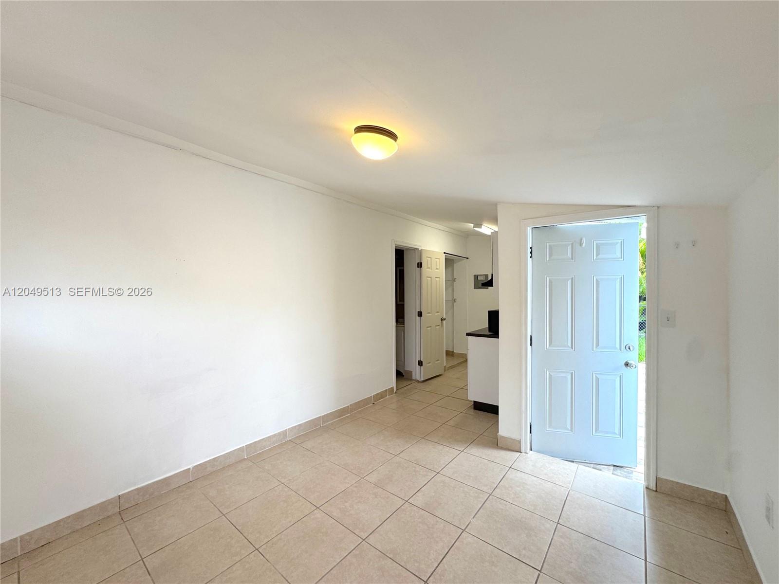A room with tiled floors, a white door, and a doorway leading to a kitchen — 2461 NW 5th St # C, Miami FL 33125, MIAMI, FL