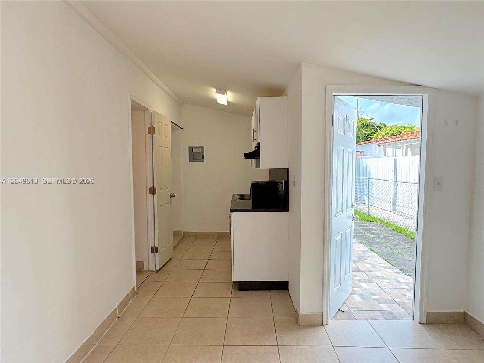 A small kitchen area with white cabinets and tile flooring leads to an exterior door — 2461 NW 5th St # C, Miami FL 33125, MIAMI, FL