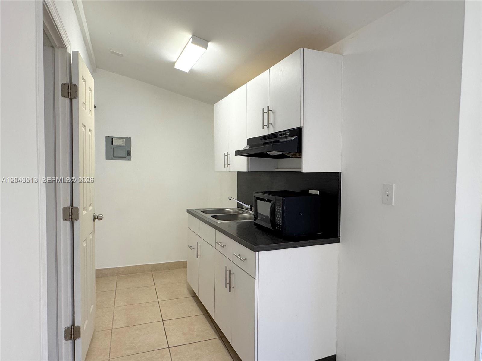 A small kitchen features white cabinets, a black countertop, and a stainless steel sink — 2461 NW 5th St # C, Miami FL 33125, MIAMI, FL