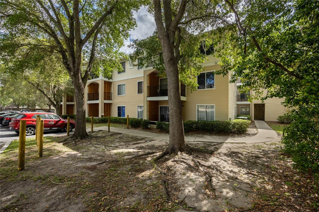 A three-story apartment building with beige siding stands behind trees and a parking lot — 3921 SW 34TH STREET UNIT 1C, GAINESVILLE, FL