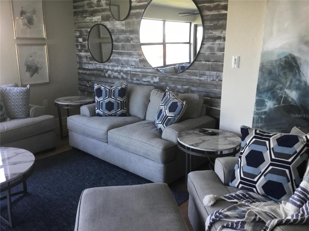 A living room features gray sofas, a wood-paneled accent wall, and round mirrors — 1571 S ATLANTIC AVENUE UNIT 204, NEW SMYRNA BEACH, FL