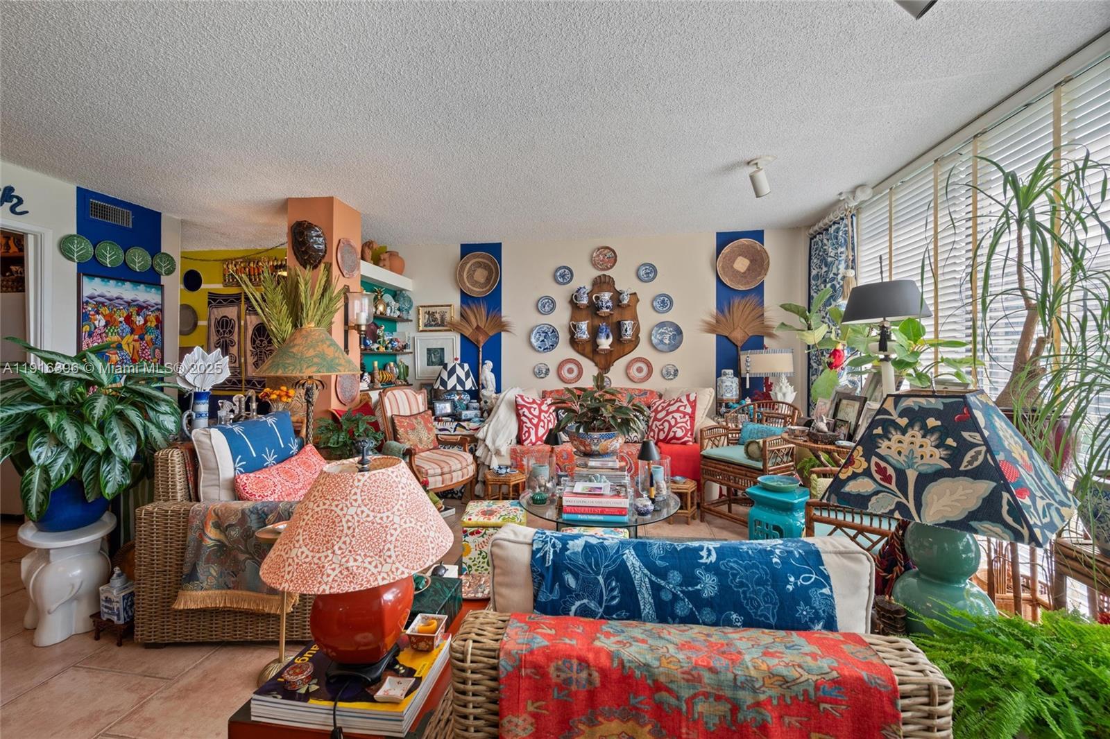 A maximalist living room features wicker furniture, patterned textiles, blue accent walls, and wall-mounted plates — 155 Sunrise Dr # 4B, Key Biscayne FL 33149, KEY BISCAYNE, FL