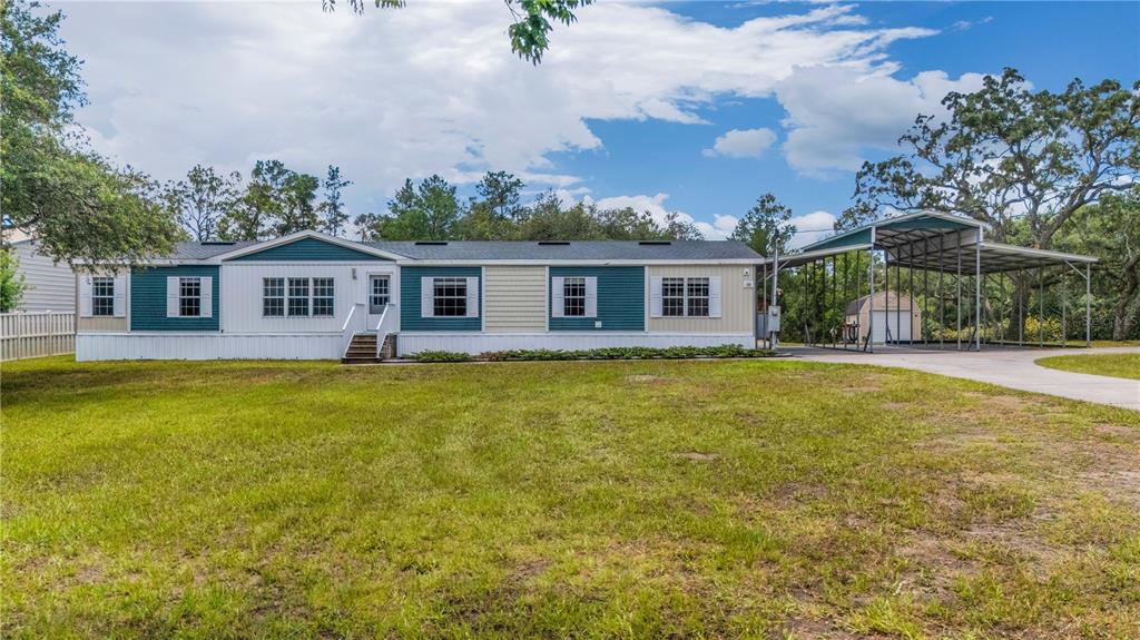 A single-story manufactured home with teal and beige siding and an attached metal carport — 6311 NODOC ROAD, SPRING HILL, FL