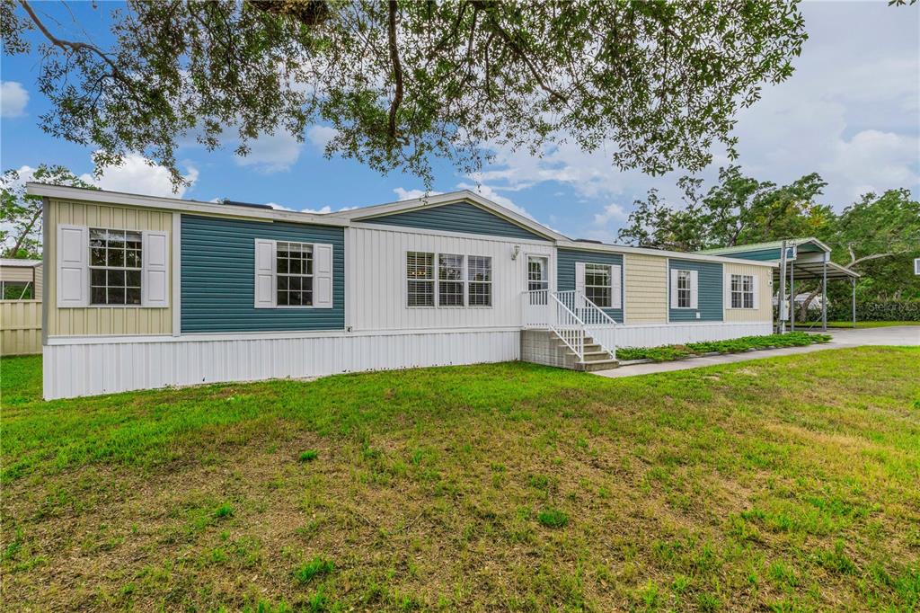 A single-story manufactured home with multi-colored siding and a covered carport under large trees — 6311 NODOC ROAD, SPRING HILL, FL