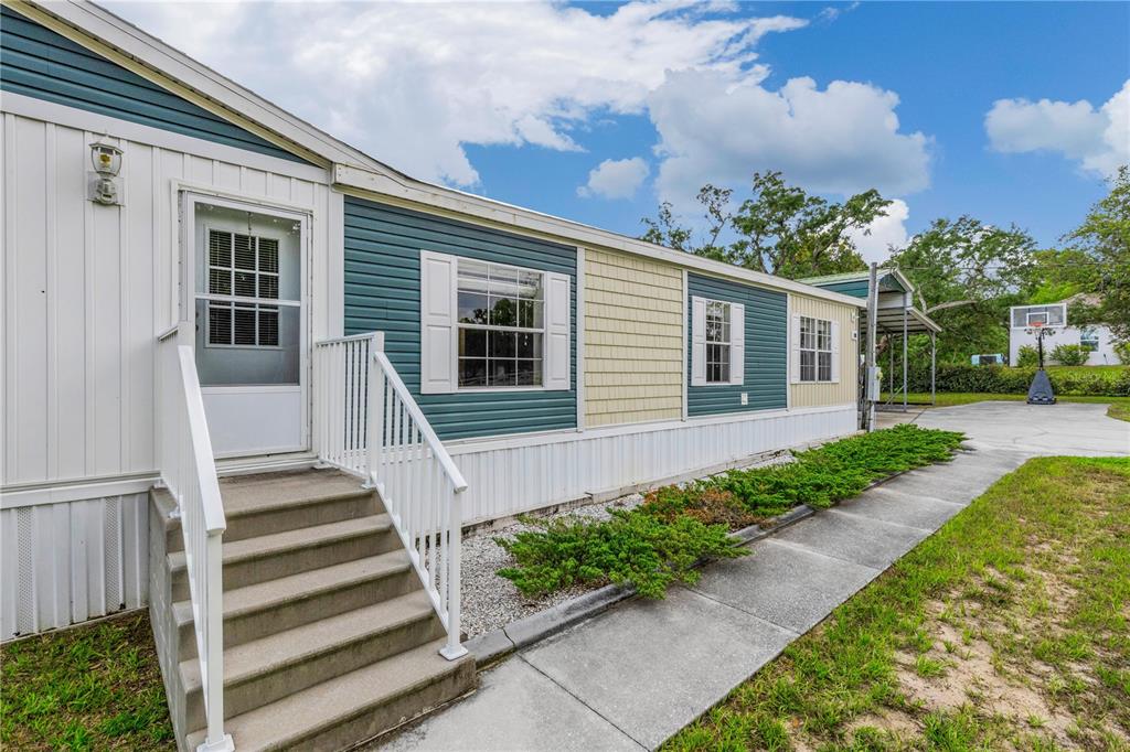 A side view of a manufactured home with white, blue, and tan siding and stairs — 6311 NODOC ROAD, SPRING HILL, FL