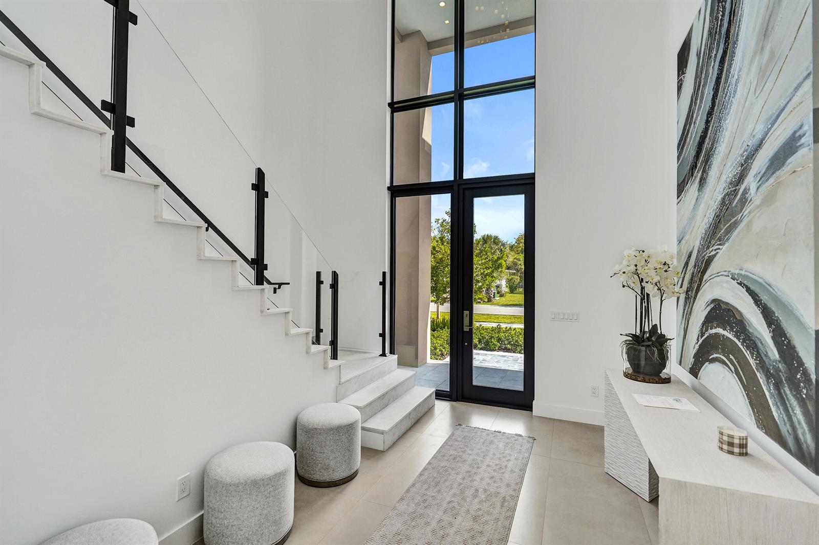 A modern entryway features a tall glass door, white walls, marble stairs, and abstract art — 235 NE 11th Street, Delray Beach FL 33444, DELRAY BEACH, FL