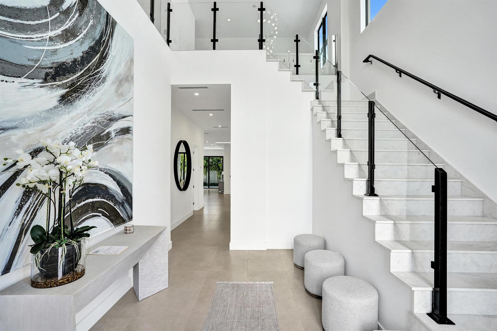 A modern entryway features a marble staircase, glass railings, white walls, and three gray ottomans — 235 NE 11th Street, Delray Beach FL 33444, DELRAY BEACH, FL