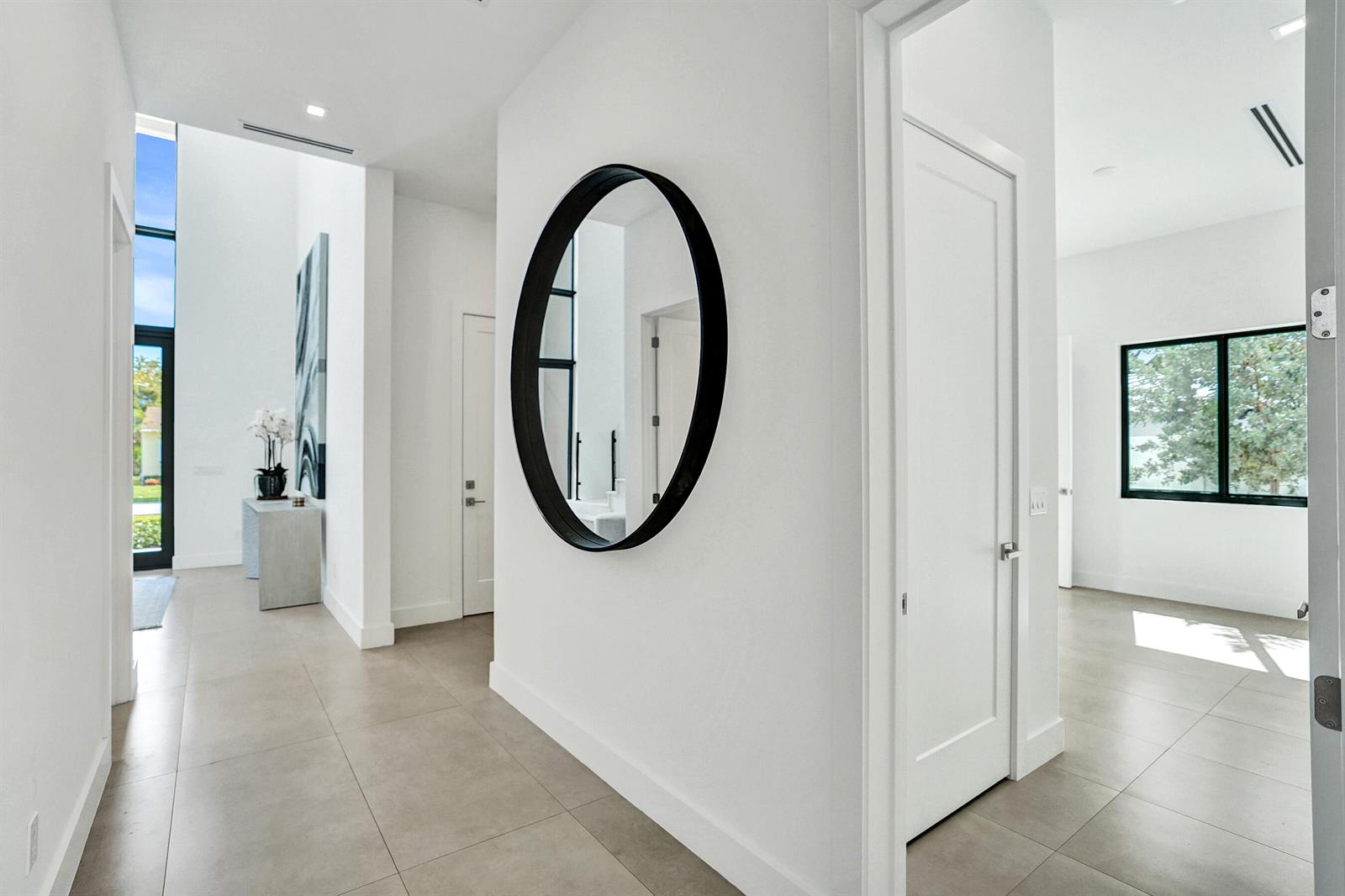 A bright hallway with white walls, large tile flooring, a round mirror, and multiple doorways — 235 NE 11th Street, Delray Beach FL 33444, DELRAY BEACH, FL