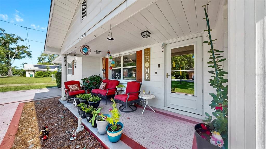 A covered front porch features red patio furniture, potted plants, and a white front door — 38919 3RD AVENUE, ZEPHYRHILLS, FL
