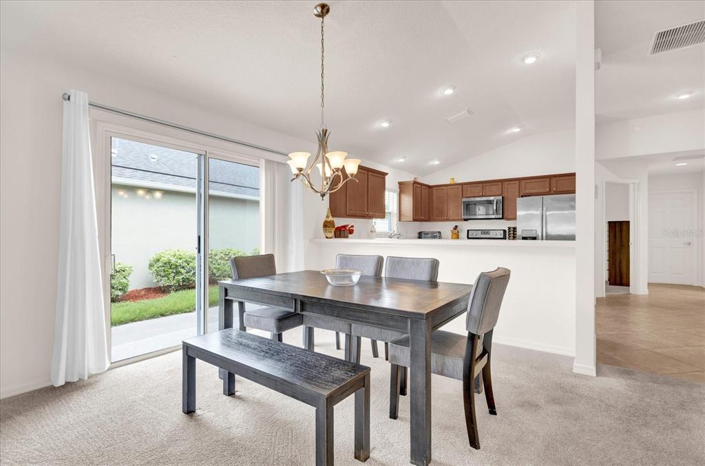 A dining area with a wooden table, bench, and chairs sits before a sliding glass door — 2850 CHARLEVOIX STREET, THE VILLAGES, FL
