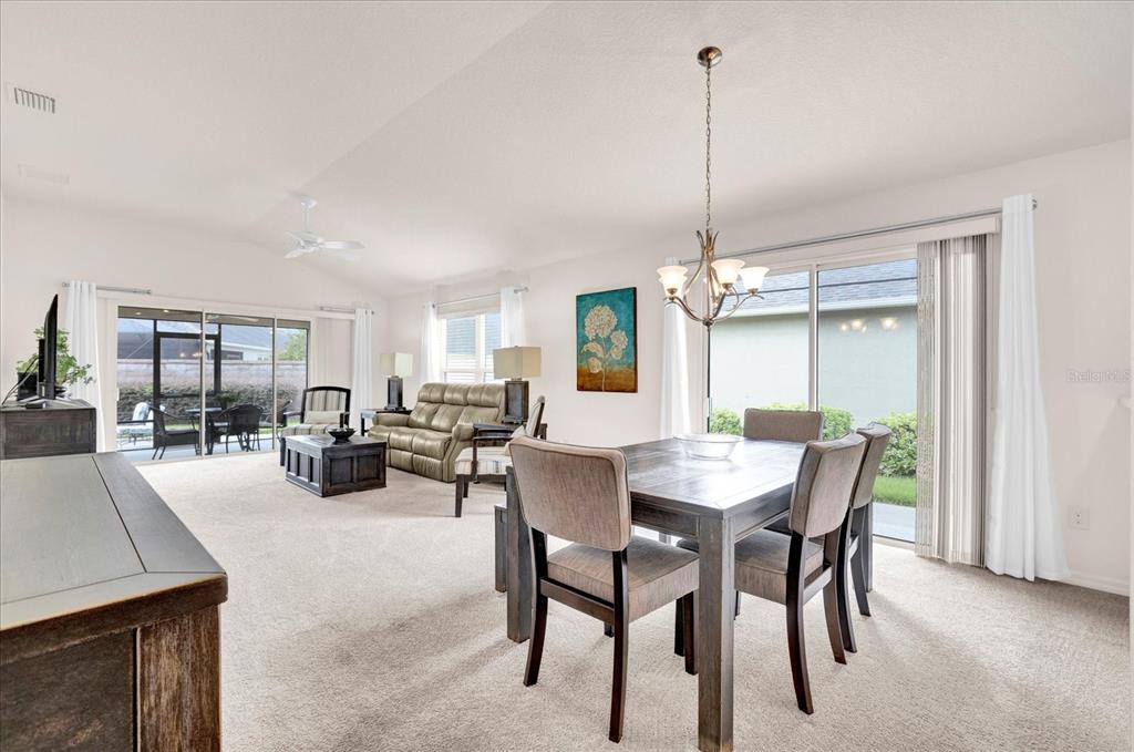 A dining area and living room with carpeted floors, sliding glass doors, and neutral walls — 2850 CHARLEVOIX STREET, THE VILLAGES, FL