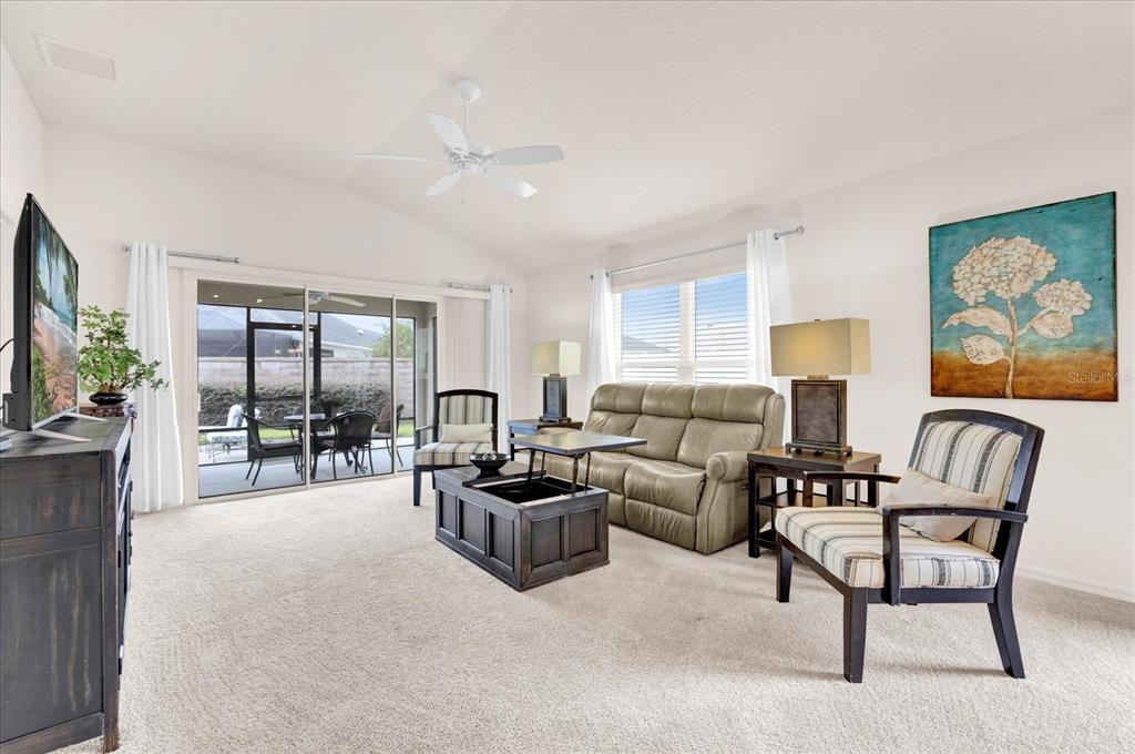 A living room features a beige sofa, two striped chairs, and a sliding glass door — 2850 CHARLEVOIX STREET, THE VILLAGES, FL