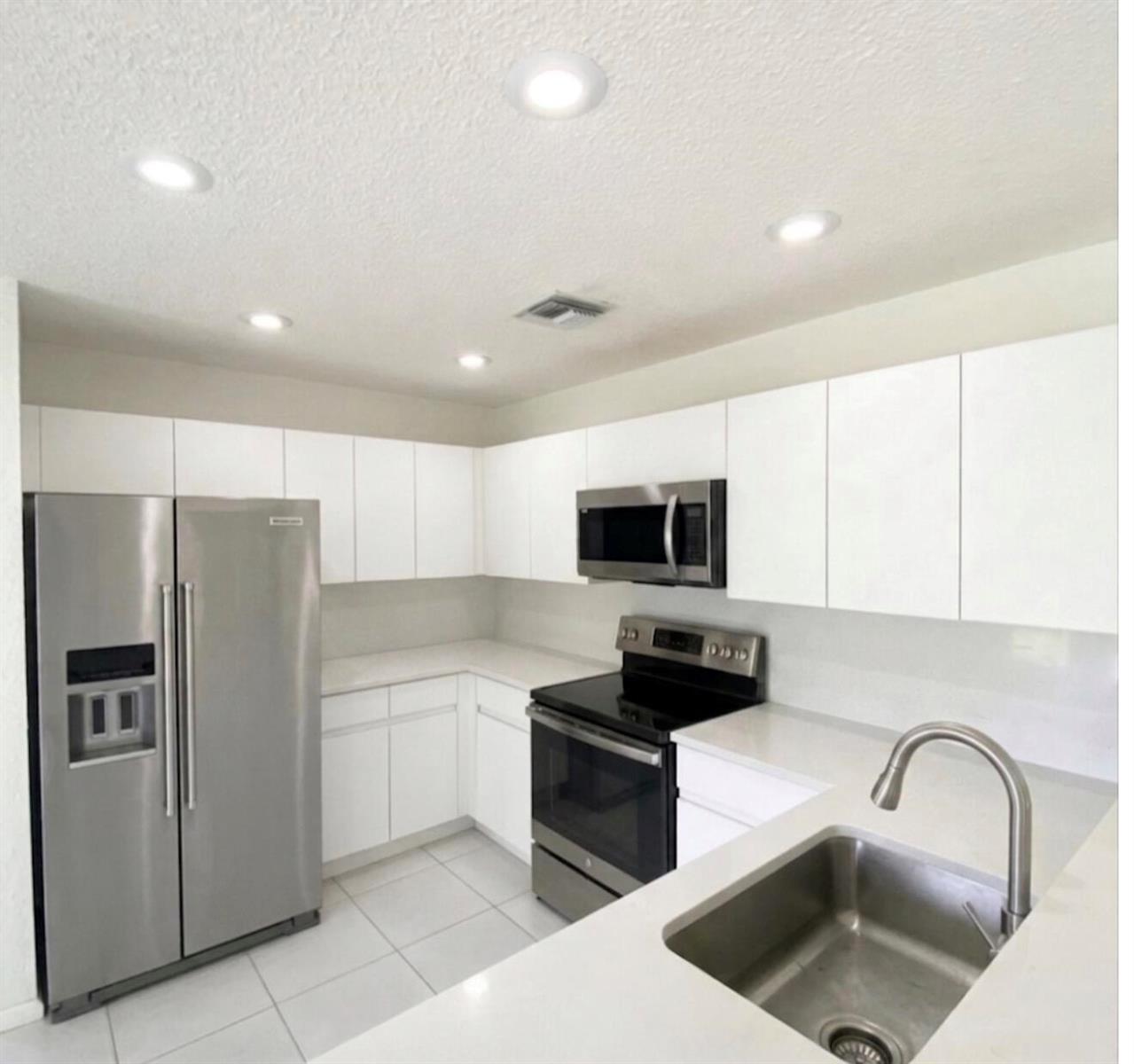 A modern kitchen features white cabinets, stainless steel appliances, and white countertops — 10533 Mendocino Lane, Boca Raton FL 33428, BOCA RATON, FL