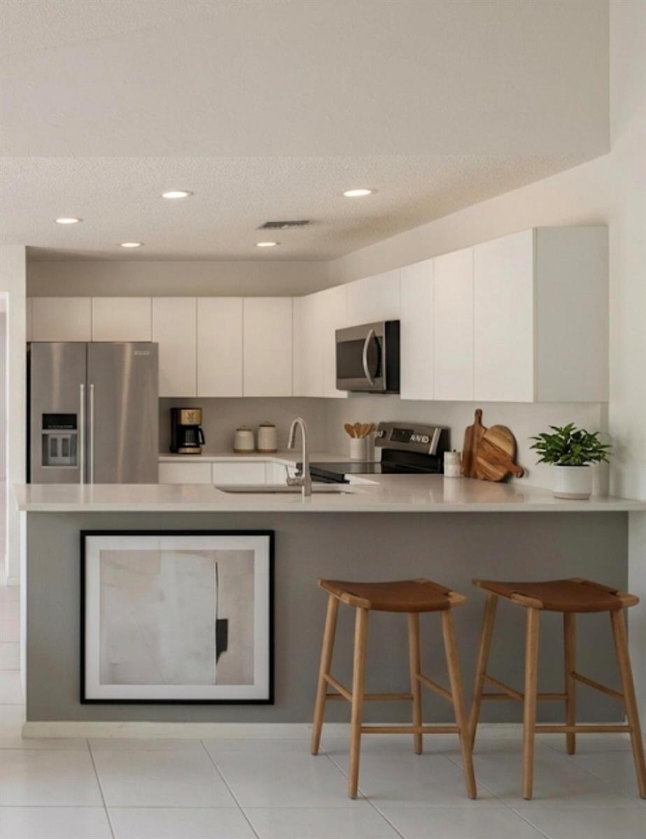 A modern kitchen features white cabinets, stainless steel appliances, a gray island, and two stools — 10533 Mendocino Lane, Boca Raton FL 33428, BOCA RATON, FL