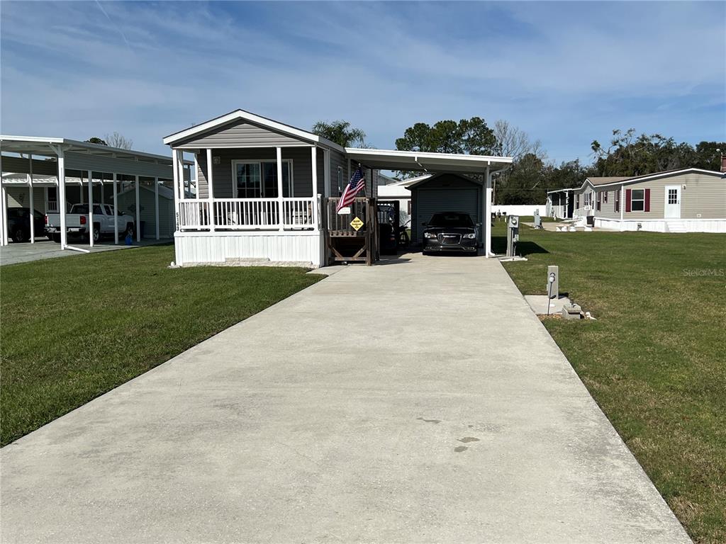 A manufactured home with a front porch, attached carport, and concrete driveway on a grassy lot — 5143 NORTHSHORE DRIVE, POLK CITY, FL